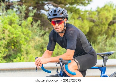 Portrait Of Professional Cyclist Resting Sitting On The Bicycle Dressed In Black Sportswear And Helmet