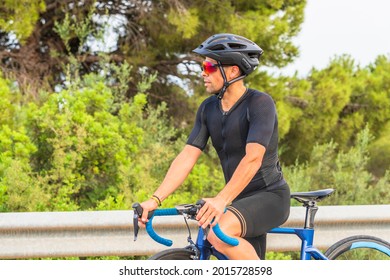 Portrait Of Professional Cyclist Resting Sitting On The Bicycle Dressed In Black Sportswear And Helmet