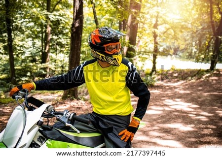 Portrait of professional dirt bike rider preparing for the motocross race through the forest.