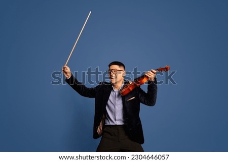 Portrait with professional, emotive musicians, violinist wearing costume holding fiddlestick and violin with happy face over blue studio background. Concept of music, art, hobby, human emotions, ad