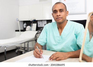 Portrait Of Professional Experienced Male Cosmetologist Working With Documents In Modern Aesthetic Medicine Office