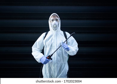 Portrait Of Professional Exterminator Holding Sprayer Equipment For Pest Control. Man In White Protective Suit Spraying Chemicals.