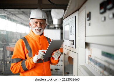Portrait of professional factory worker or engineer in high visibility jacket and hardhat standing in control room of industrial production hall. Factory interior. - Shutterstock ID 2122082663