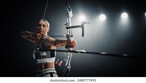 Portrait of Professional Female Archer Aiming an Arrow at a Target with a Compound Bow. Strong Athlete is Fully Equipped and Protected with Chest and Arm Guards, Preparing For Tournament - Powered by Shutterstock