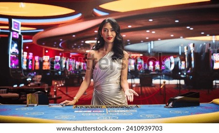 Portrait of a Professional Female Croupier Looking at the Camera and Welcoming You to a Table. Beautiful Asian Dealer in Silver Dress Dealing Playing Cards in a Casino for a Game of Baccarat