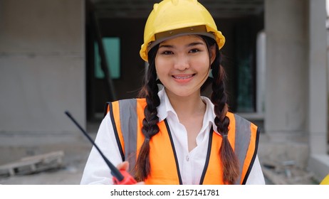 Portrait of professional female engineer worker with safety uniform holding walkie-talkie to talk with team opening blueprint to check project plan looking at camera with confident smile