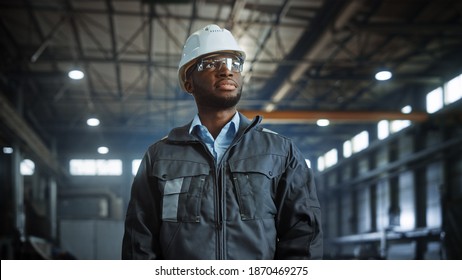 Portrait of Professional Heavy Industry Engineer Worker Wearing Uniform, Glasses, Hard Hat in Steel Factory. Smiling African American Industrial Specialist Standing in Metal Construction Manufacture.