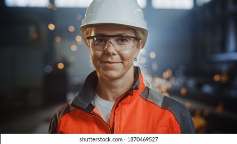 Portrait of a Professional Heavy Industry Engineer Worker Wearing Uniform, Glasses and Hard Hat in a Steel Factory. Beautiful Female Industrial Specialist Standing in Metal Construction Facility.