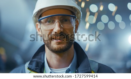 Portrait of Professional Heavy Industry Engineer / Worker Wearing Safety Uniform, Goggles and Hard Hat Smiling. In the Background Unfocused Large Industrial Factory where Welding Sparks Flying Stock photo © 