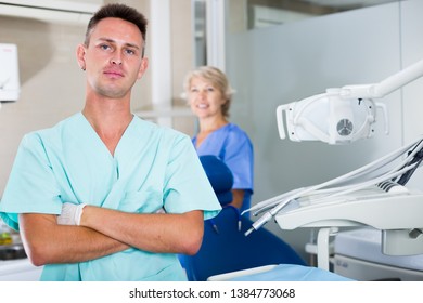 Portrait of professional male dentist with arms crossed with dental assistant background