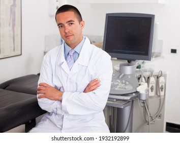 Portrait Of Professional Male Sonographer Sitting With Arms Crossed In Medical Diagnostics Office