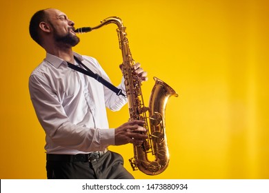 Portrait of professional musician saxophonist man in  white shirt plays jazz music on saxophone, yellow background in a photo studio, side view - Powered by Shutterstock