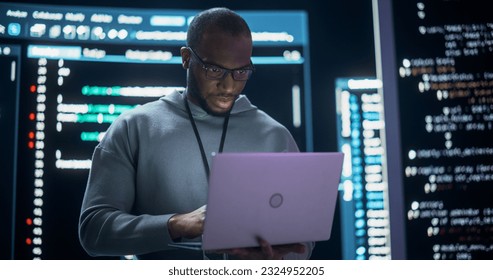 Portrait of Professional Programmer Developing a Big Data Interface Software Project.Young Black Man Working on Laptop Computer, Looking at Big Digital Screen Displaying Back-end Code Lines - Powered by Shutterstock