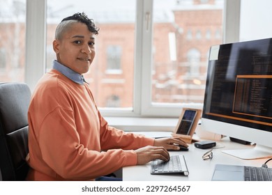 Portrait of professional programmer smiling at camera while writing codes on computer sitting at his workplace