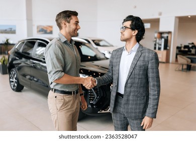 Portrait of professional salesman in business suit shaking happy client hand and talking. Stylish male car dealer serving smiling customer in showroom. Car business, trading, dealership. - Powered by Shutterstock