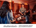 Portrait of professional talented guitarist standing at music recording studio and playing electric guitar while drummer in a blurry foreground is sitting and playing drums.Band making music at studio