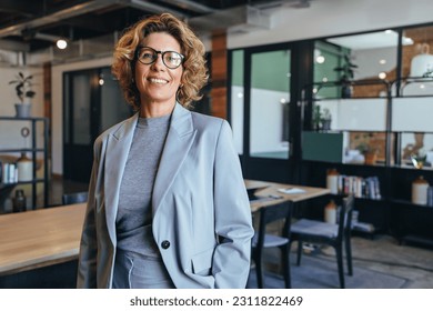 Portrait of a professional woman in a suit standing in a modern office. Mature business woman looking at the camera in a workplace meeting area.
