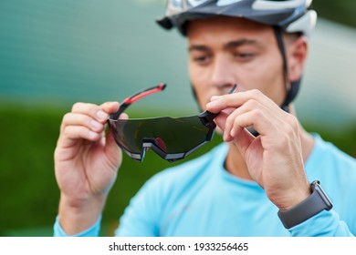 Portrait of professional young male cyclist wearing suit holding, putting on protective glasses while getting ready for cycling outdoors