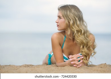 Portrait In Profile Of A Young Beautiful Blonde With Flowing Hair On The Beach. A Gorgeous Caucasian Female Lies On The Beach And Enjoys A Sunny Afternoon And The Sound Of Waves.