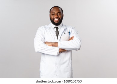 Portrait of proud and confident african-american male doctor in white coat, cross hands chest and smiling pleased, boastful over his nurses and best hospital in town, taking care of patients