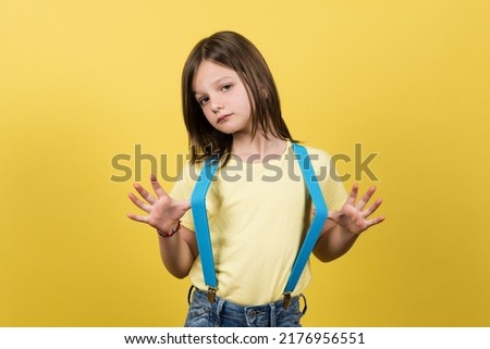 Portrait of proud little girl wearing suspenders looking at camera isolated on yellow background.