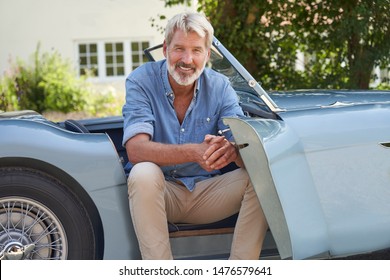 Portrait Of Proud Mature Man Sitting In Restored Classic Sports Car Outdoors At Home      