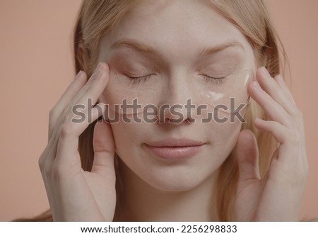 Portrait of pure natural beautiful 20s Caucasian female using eye patches against pastel colored background