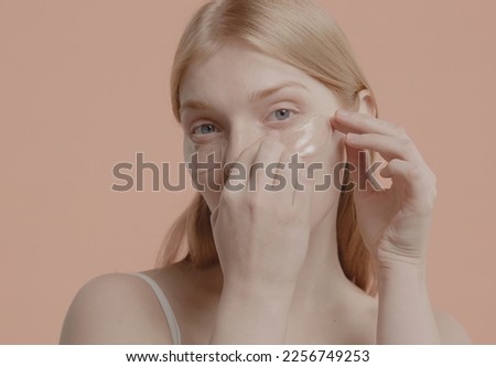 Portrait of pure natural beautiful 20s Caucasian female using eye patches against pastel colored background