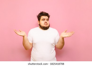 Portrait of puzzled fat man with shocked face on pink background, looking to the side and spreading his hands to the sides. Funny puzzled young man looking away on a pink background.