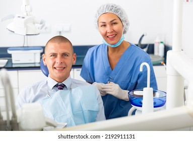 Portrait Of A Qualified Asian Woman Dentist With A Smiling Man Patient Sitting In A Dental Chair At The Clinic