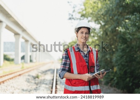 Portrait of railway female engineer in vest and helmet safety holding tablet working and maintenance railroad track for rail train transport