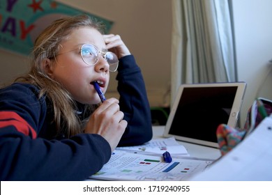 Portrait Of A Real 10 Year Old Girl With Glasses And Thinking Face Expression Doing Homeschooling, Learning At Home, Doing Homework While Chewing On A Pen                                   