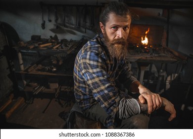 Portrait of a real Brutal blacksmith of a man with a beard after working in his workshop against the background of a burning flame. Portrait of a profession. - Powered by Shutterstock