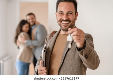 Portrait of a real estate agent in the apartment for sale or for rent.  A young married couple standing in the background. Real estate concept. - Shutterstock ID 2319618199