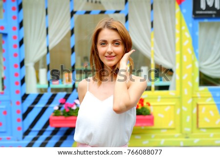 Portrait of red haired woman against multicoloured blue and yellow wall, windows with curtains and pink flower pot.