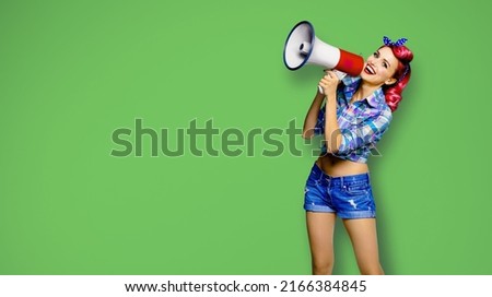 Portrait of red purple haired woman holding megaphone, shout advertising something. Girl in pin up style wear. Isolated over green background with mock up. Female model in retro fashion. Sale offer ad