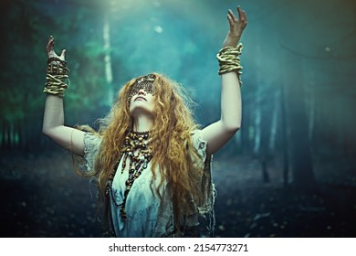 Portrait Of A Red-haired Druid Woman With A Mask On Her Eyes Standing In A Gloomy Forest And Performing An Ancient Druidic Ritual. Paganism. Halloween. 