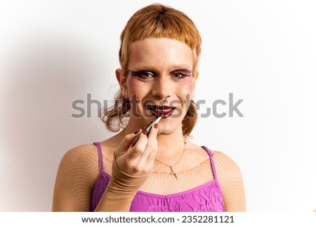 Portrait of a red-haired non-binary person is posing on a white background while painting his lips and looking at the camera happily. Concept of people is not identified with any gender. Men in makeup