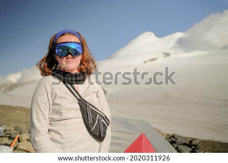 Portrait of a red-haired woman in a ski mask. Tourist climber on the background of Mount Kazbek. Climbing Kazbek from the north, from the side of Russia.
