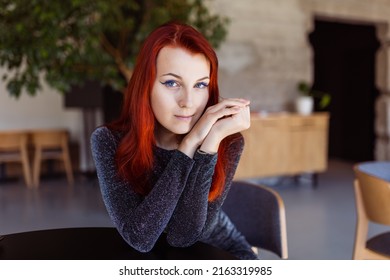 portrait of a red-haired young girl with blue eyes. Attractive redhead girl with pale skin and natural make-up posing for the camera in a cafe - Shutterstock ID 2163319985