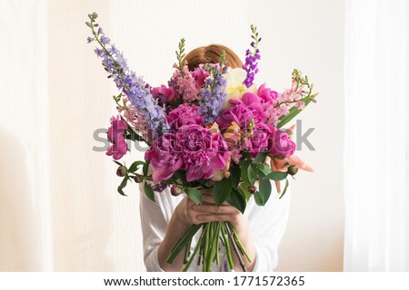 A portrait of redhead girl standing with a beautiful spring bouquet of pink flowers hiding her face. Floristics concept 
