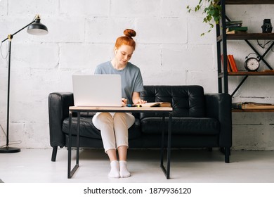 Portrait Of Redhead Young Woman Student Noting Into The Workbook Important Information From Book In Preparation For Lessons At Table With Laptop. Lady Doing Paperwork With Book In Home Office