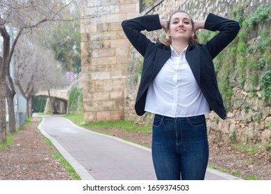 Portrait Of Relaxed Bussiness Woman Model Touching His Head With Both Hands, Having Time For Rest, Looks Quiet And Peaceful. Slender Charismatic Man Poses, In The Park, White Shirt And Black Jacket, L