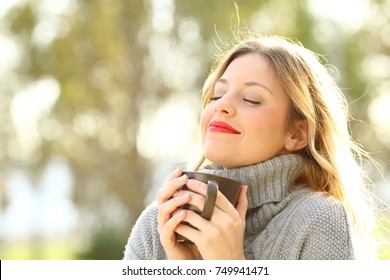 Portrait of a relaxed girl wearing jersey holding a cup of coffee and breathing outdoors in a park in winter