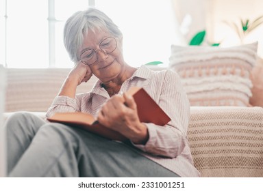 Portrait of relaxed retired senior woman sitting on the floor at home while reading a book enjoying free time and retirement - Powered by Shutterstock