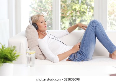 Portrait Of Relaxed Woman With Headphone Sitting At Sofa And Listening Music On Digital Tablet.