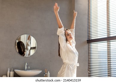 Portrait Of Relaxed Young Lady In White Silk Robe Stretching In Luxury Bathroom, Smiling Millennial Female Enjoying Morning Time, Standing With Raised Arms By Panoramic Window At Home, Copy Space - Powered by Shutterstock