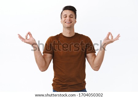 Portrait of relieved and happy, healthy young man smiling with calm and relaxed face, closed eyes, hold hands sideways in nirvana lotus pose, meditating and breathing freely, white background