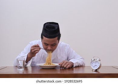 Portrait Of Religious Asian Man In Koko Shirt Or White Muslim Shirt And Black Cap Eating Instant Noodles For Suhoor To Be Strong During Fasting From Dawn To Dusk In Ramadan Month