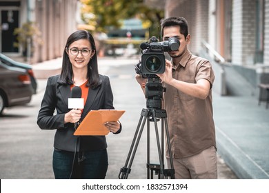Portrait reporter woman holding a microphone with reporting news and cameraman shooting outdoor in Bangkok, Thailand.